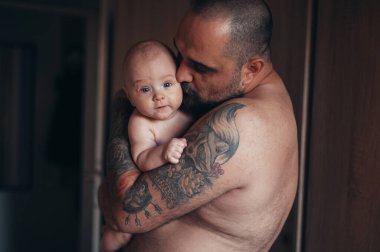 Dövmeli sakallı baba evdeyken oğluyla bebek bezi ile oynuyor.