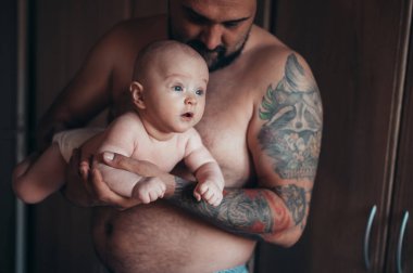 Dövmeli sakallı baba evdeyken oğluyla bebek bezi ile oynuyor.