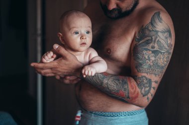 Dövmeli sakallı baba evdeyken oğluyla bebek bezi ile oynuyor.