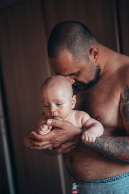 Dövmeli sakallı baba evdeyken oğluyla bebek bezi ile oynuyor.