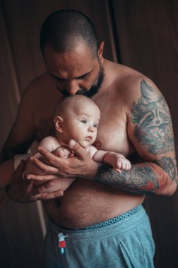 Dövmeli sakallı baba evdeyken oğluyla bebek bezi ile oynuyor.