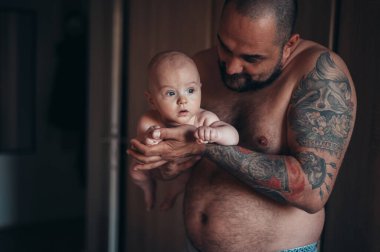 Dövmeli sakallı baba evdeyken oğluyla bebek bezi ile oynuyor.