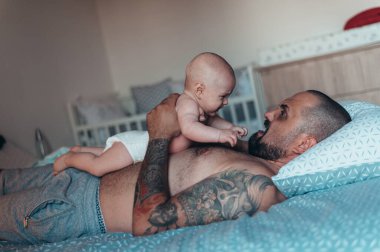 Dövmeli sakallı baba evdeyken oğluyla bebek bezi ile oynuyor.