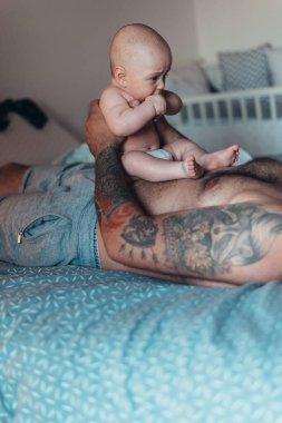 Dövmeli sakallı baba evdeyken oğluyla bebek bezi ile oynuyor.