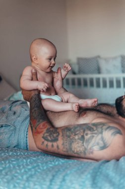 Dövmeli sakallı baba evdeyken oğluyla bebek bezi ile oynuyor.