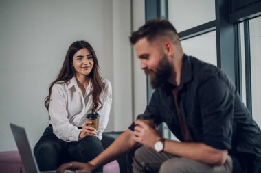 İki genç iş adamının portresi. Laptop kullanıyorlar ve ofiste otururken kahve içiyorlar. İki iş arkadaşı toplantı sırasında tartışıyorlar. Beyaz bir kadına odaklan.