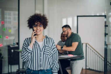 Kendine güvenen kadın iş lideri kameraya bakıyor ve takım toplantısında akıllı telefon kullanarak ofiste dikiliyor. Yönetim kurulundaki meslektaşlarıyla birlikte kendine güvenen bir iş kadınının portresi..