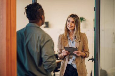 İki genç iş adamı toplantı odasında dikilirken dijital tablet kullanıyorlar. İki iş arkadaşı çalışırken fikirler ve çözümler hakkında tartışıyorlar..