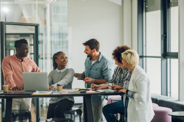 Modern, aydınlık ofis içi bir toplantıda çok ırklı bir iş ekibi kuracağız. Kadın takım lideri çeşitli meslektaşlarına projesini sundu.