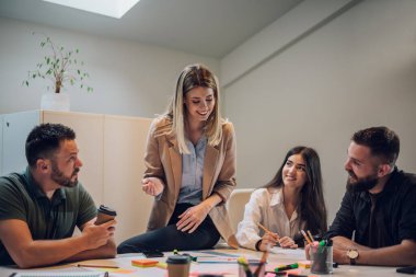 Modern, endüstriyel tasarım ofisinin içindeki bir toplantıda iş ekibi. Takım lideri projeyi meslektaşlarına sundu. Masada oturan sarışın kadına odaklan..