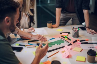 Bir grup genç iş arkadaşı toplantı sırasında şirket projeleri hakkında konuşuyor. Takım çalışması konsepti. İş arkadaşları yeni projelerinde birlikte çalışıyorlar. Masadaki satış raporuna odaklan.