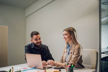 İki genç iş adamı toplantı odasında yeni projeleri hakkında konuşurken dizüstü bilgisayar kullanıyorlar. İki iş arkadaşı toplantı sırasında tartışıyorlar. Erkek ve bayan meslektaşlar birlikte çalışıyor..