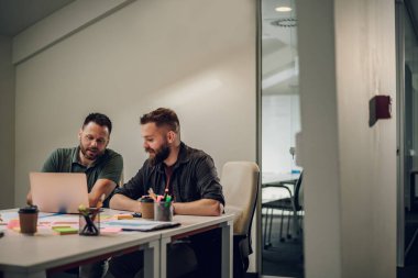 İki genç iş adamı toplantı odasında toplanırken dizüstü bilgisayar kullanıyor. İki iş arkadaşı yeni projeleri hakkında tartışıyorlar. Modern bir ofiste çalışan iki erkek..
