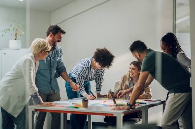 Modern, aydınlık ofis içi bir toplantıda çok ırklı bir iş ekibi kuracağız. Kadın takım lideri çeşitli meslektaşlarına projesini sunar. Gülümseyen takım arkadaşları iş yerindeki toplantı odasında.