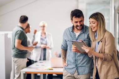 Dijital tablet üzerinde çalışan iki iş arkadaşının fotoğrafı. Yaratıcı yöneticiler bir ofiste dijital tablet kullanarak buluşuyorlar ve gülümsüyorlar..