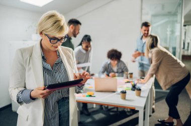 Ofisteki bir toplantıda arka planda meslektaşlarıyla gülümseyen güzel bir iş kadınının portresi. İş kadını takım lideri konsepti. İş yerinde dijital tablet kullanırken poz vermek.