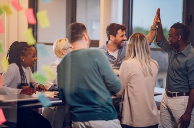 Çeşitli yaratıcı iş adamları modern bir şirketin toplantı odasında birlikte çalışıyorlar. Beyin fırtınası konsepti. Ofis hayatı. Çok ırklı iş arkadaşları. Çıkartmalı cam bir duvarın içinden bak.