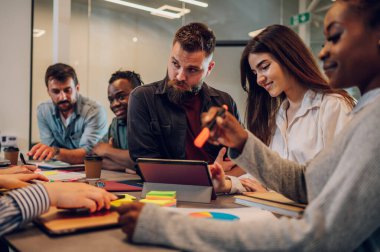 Çeşitli meslektaşlar, yeni projeleri için yeni fikirleri tartışırken ofiste toplandı. Dijital tablet kullanan sakallı beyaz bir adama odaklan. .
