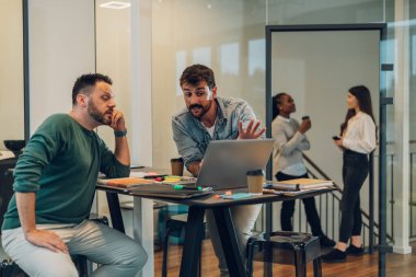 İki iş adamı proje stratejisi hakkında konuşuyor ve toplantı odasında dizüstü bilgisayar kullanıyor. Modern işyerinde çalışan iki iş arkadaşı mali veri raporları hakkında konuşurken....