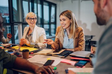 Bir grup çok ırklı genç meslektaşın toplantı odasında şirket projeleri hakkında konuşuyorlar. Takım çalışması konsepti. Çeşitli iş arkadaşları birlikte çalışıyor. Güzel beyaz bir kadına odaklan..