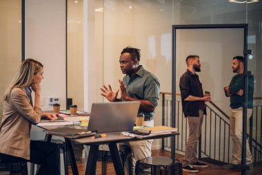 Ofiste sohbet eden ve dizüstü bilgisayar kullanan iki farklı iş adamı. Heyecanlı beyaz kadın fikirleri paylaşıyor ya da siyahi erkek iş arkadaşıyla iş planı yapıyor. İş molası kavramı. Çok ırklı takım.