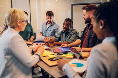 Çeşitli ofisteki neşeli insanlar ekip çalışmasını konuşarak ve eğlenerek yapıyor. Çok ırklı iş arkadaşları ofiste beyin fırtınası yaparken eğleniyor. Takım çalışması konsepti.