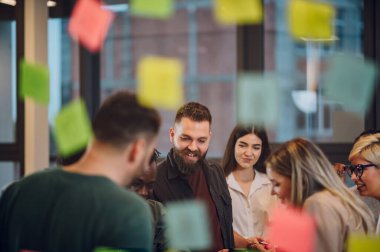 Modern bir ofiste eğlenceli, çok ırklı, yaratıcı genç insanlar. Yaratıcı ortak çalışma alanında birlikte çalışan bir grup farklı iş adamı. Eğlenceli insanlarla çalışmak. Camdan bir duvarı izle.