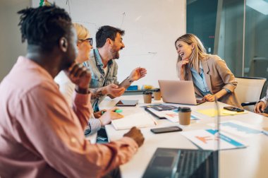 Modern, endüstriyel tasarım ofisinin içindeki bir toplantıda çok ırklı bir iş ekibi. Kadın takım lideri projeyi çeşitli meslektaşlarına sundu. Sarışın bir kadına odaklan..