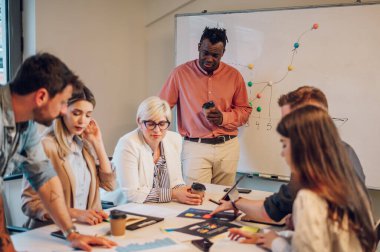 Çok kültürlü profesyonel proje yöneticileri grubu toplantı salonunda müzakere ediyor. Afrikalı Amerikalı patron yaratıcı çeşitli takımlarla projelerinde iş stratejisi kavramını tartışıyor..