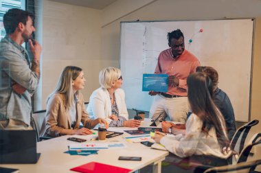 Çeşitli ofisteki neşeli insanlar ekip çalışmasını konuşarak ve eğlenerek yapıyor. Mutlu çok ırklı iş arkadaşları ofiste birlikte çalışırken eğleniyor. Takım çalışması konsepti. Satış grafikleri gösteriliyor.