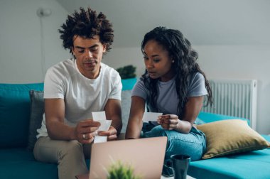 Genç Afro-Amerikan çift evde harcamalarını ve ev bütçelerini hesaplarken dizüstü bilgisayar ve kredi kartı kullanıyor. İnternetten alışveriş. Muhasebeyi ve faturaları kontrol ediyorum..