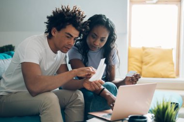 Evde dizüstü bilgisayarı ve kredi kartıyla oturan ve aylık faturaları ya da online alışverişi ödeyen Afro-Amerikan çift. Çevrimiçi bankacılık başvurusu, vergileri gözden geçirme, iç faturalar.