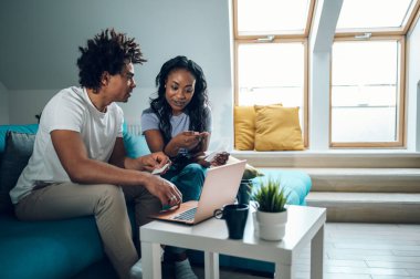 Evde dizüstü bilgisayarı ve kredi kartıyla oturan ve aylık faturaları ya da online alışverişi ödeyen Afro-Amerikan çift. Çevrimiçi bankacılık başvurusu, vergileri gözden geçirme, iç faturalar.