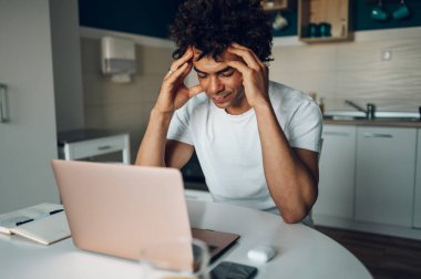 Genç Afrikalı Amerikalı iş adamı dizüstü bilgisayar kullanırken yorgun ve stresli ve evdeki mutfakta uzaktan çalışıyor. Evden çalışıyorum. Son teslim tarihi.