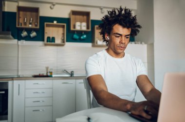 Yakışıklı Afro-Amerikan erkeği evde bir mutfakta otururken ya da çalışırken dizüstü bilgisayar kullanıyor. Uzaktan kumandalı başarılı bir iş. Evden bir proje üzerinde çalışıyorum..