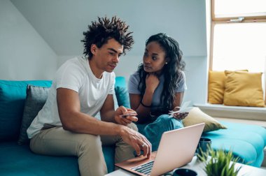 Evde dizüstü bilgisayarı ve kredi kartıyla oturan ve aylık faturaları ya da online alışverişi ödeyen Afro-Amerikan çift. Çevrimiçi bankacılık başvurusu, vergileri gözden geçirme, iç faturalar.
