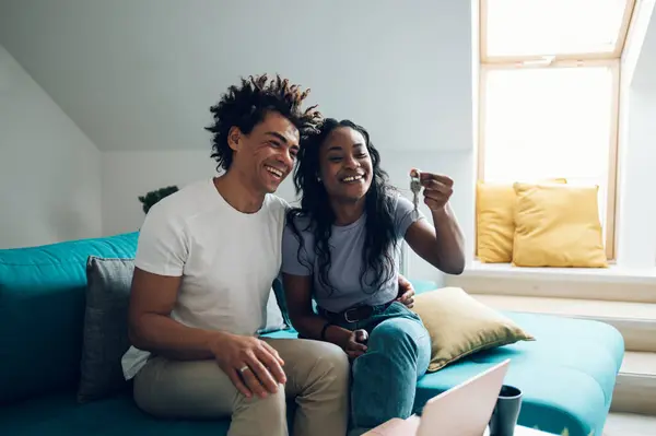 Young african american couple holding home keys in their new apartment after buying real estate. Excited homeowners.