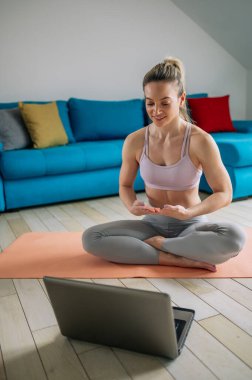 Fitness kadın blogcusu bilgisayarına video kaydediyor ve evde oturma odasında antrenman yapıyor. Yaşam tarzını etkileyen spor ve eğlence konsepti.