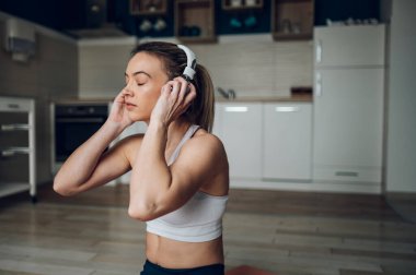 Güzel bir kadın evde yoga yapıyor ve dinlenirken kulaklıkla müzik dinliyor. Sakinleştirici müzik vücudunu sakinleştirir..