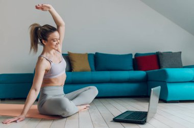 Fitness kadın blogcusu bilgisayarına video kaydediyor ve evde oturma odasında antrenman yapıyor. Yaşam tarzını etkileyen spor ve eğlence konsepti.