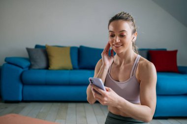 Hava podu ve akıllı telefon kullanan güzel bir atletik kadın evde antrenman yaptıktan sonra müzik dinleyip dinleniyor. Antrenman molasında akıllı telefon kullanmak.