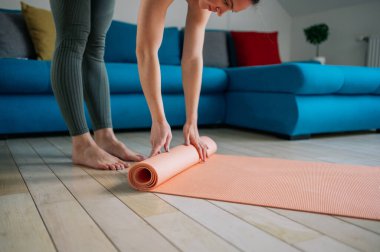 Genç kadın, evde yoga yapmadan önce ya da sonra ahşap zeminde pembe egzersiz paspası katlıyor. Fitness, pilates ya da yoga ekipmanları.