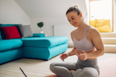 Güzel bir genç kadın evde antrenman yapıyor ve oturma odasında dizüstü bilgisayar başında yoga minderinde vücut esnetiyor. Evde egzersiz yap..