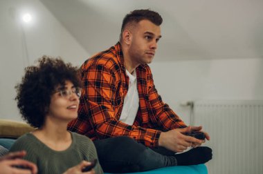 Evde video oyunu oynayan ve eğlenen çok ırklı bir arkadaş grubu. Gençler internetteki yeni teknoloji konsoluyla eğleniyorlar. Elinde joystick tutan, kareli gömlekli genç bir adama odaklan..