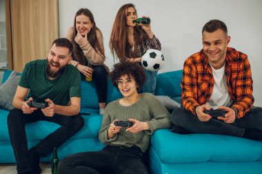 Gülümseyen bir grup arkadaş evde oyun oynuyor ve eğleniyorlar. Gençler internetteki yeni teknoloji konsoluyla eğleniyor.