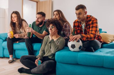 Bir grup neşeli arkadaş evde oturup, bira içerken ve tezahürat yaparken televizyonda maç izliyorlar. Arkadaşlık, spor ve eğlence konsepti.