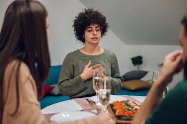 Neşeli bir grup mutlu arkadaş evde yemek yiyor. Arkadaş toplantısı. Bir grup mutlu insan konuşup yemek yiyor. Mutlu arkadaşlar, güzel yemekler ve içecekler..