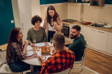 Mutfak masasında birlikte otururken bir grup neşeli genç akşam yemeğinin tadını çıkarıyor. İçip eğlenirken yemek yerken arkadaşlarımla harika vakit geçiriyorum.