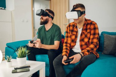 Erkek en iyi arkadaşlar sanal gerçeklik kulaklıklarıyla eğlenirken çevrimiçi video oyunları oynuyorlar ve evde birlikte vakit geçiriyorlar..