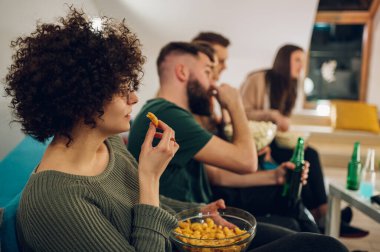 Neşeli bir grup arkadaş evde kanepede atıştırmalıklarla film izliyorlar. Televizyonda komedi filmi izliyorum. Arkadaşlar, ev eğlencesi, boş zaman konsepti.